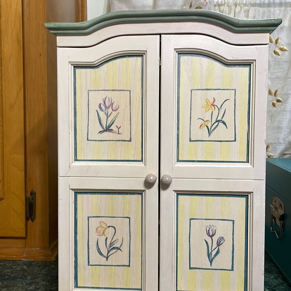 Jewelry cabinet 2 door opens.  Inside is a mirror and shelves. Antique cream.